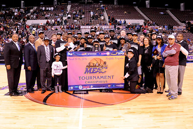 2014 MEAC Tournament champions North Carolina Central pose at center court behind championship banner with coaching staff.