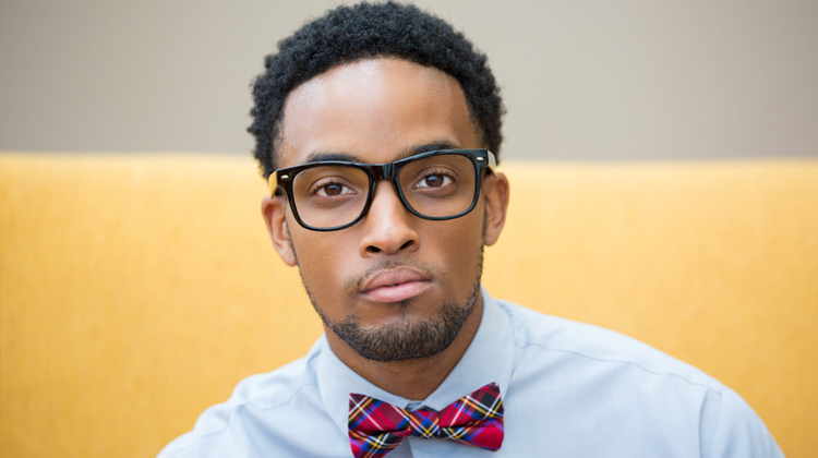A close up portrait black male college student with black glasses and bow tie, isolated yellow white background.