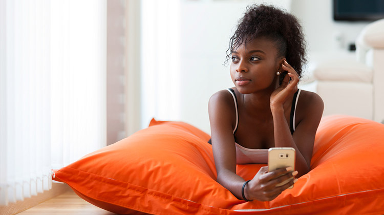 African American woman is sending a text message on a mobile phone at home after returning home from college.