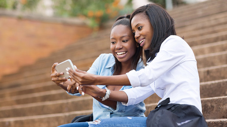 Female African American roommates in college using cell phone to take a selfie on campus