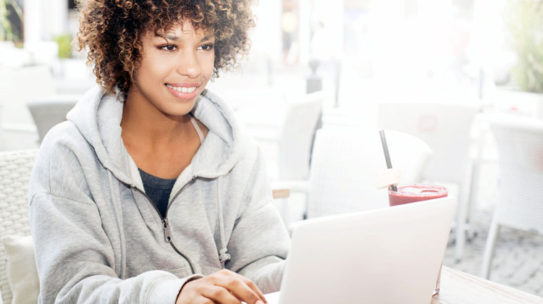 Young beautiful african american HBCU student using laptop, sitting at cafe work on a annotated bibliography for a research paper.